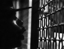 A drill instructor barks at a young man behind bars.
